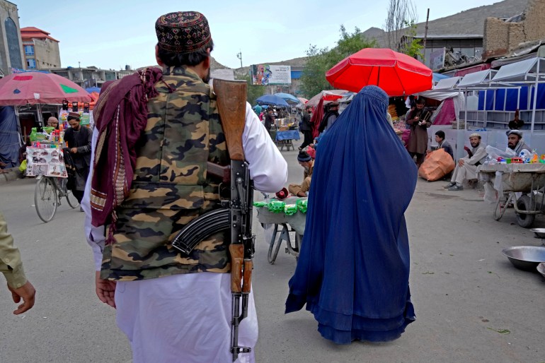 A woman wearing a burka walks through the old market as a Taliban fighter stands guard, in downtown Kabul