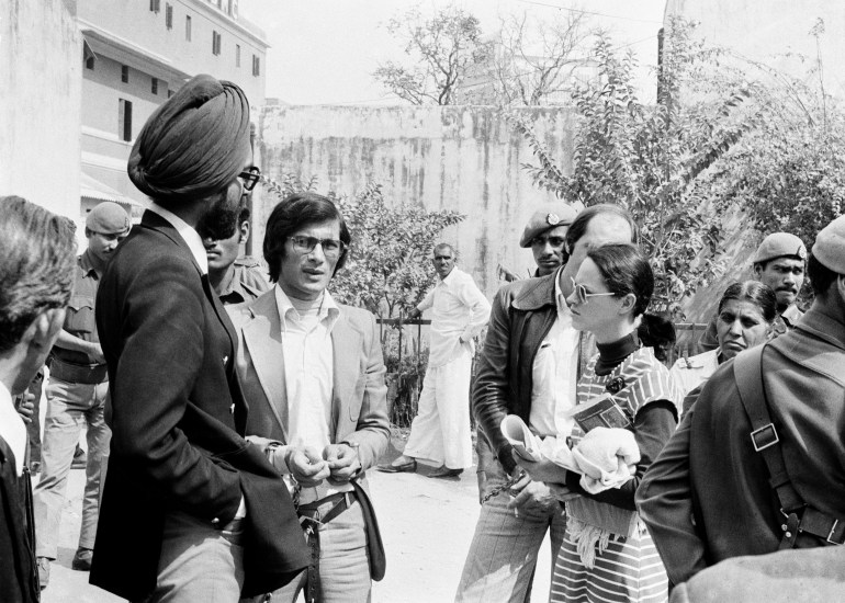 Charles Sobhraj, center, the alleged leader of an Asian murder ring, and his girlfriend Marie-Andree Leclerc, striped dress, wait outside of court during one of their appearances, in New Delhi, India, Feb. 24, 1977. They are in court for preliminary hearings into whether they should be charged with the drugging, robbing and murder of foreign tourists. They were arrested here last July and are also wanted by authorities in Thailand. (AP Photo)