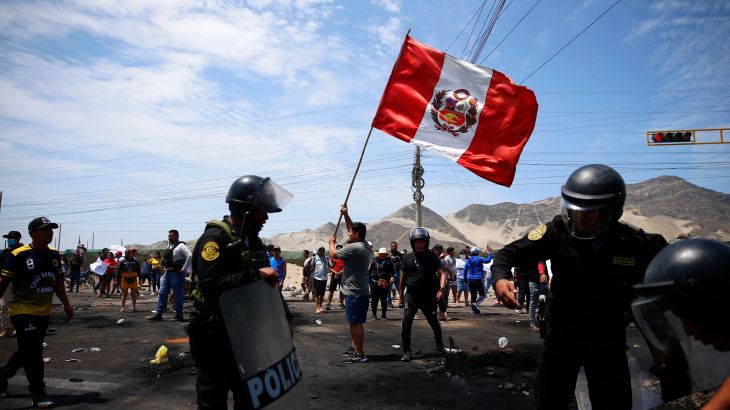 Supporters of Castillo wave a Peruvian flag during a protest. There are armed police in the foreground.