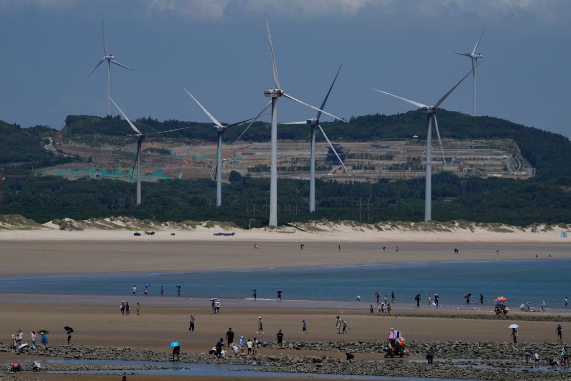 Beachgoers walk near wind turbines along the coast of Pingtan in Southern China