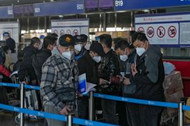 Masked travellers check their passports as they line up at the international flight check-in counter at the Beijing international airport