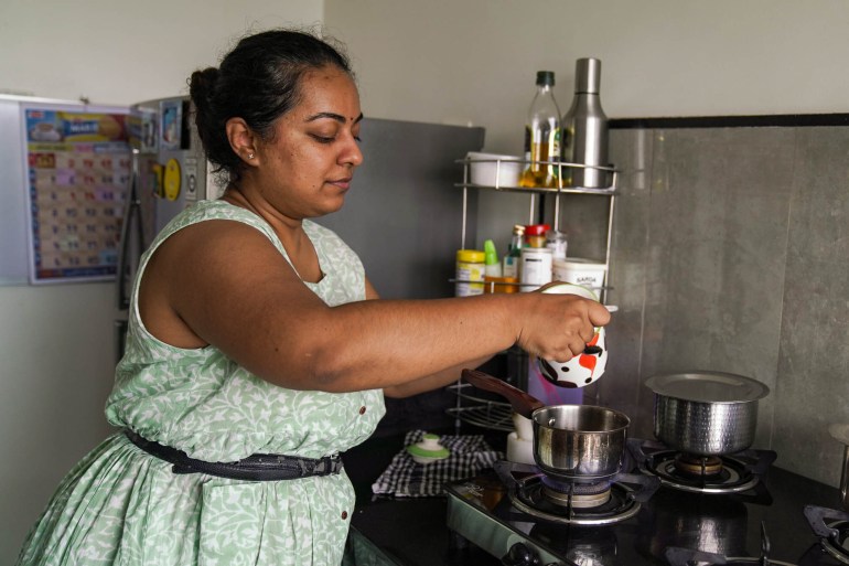 Akanksha standing at her stove, measuring and pouring