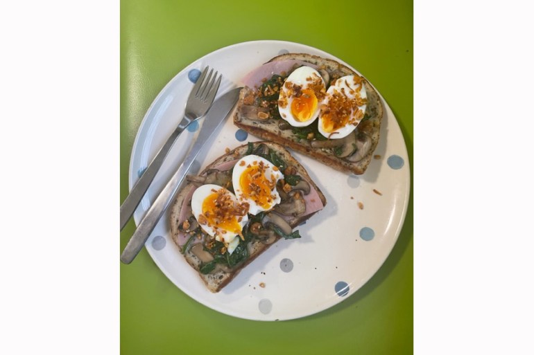a white plate with blue spots sits on a green background. On it are two slices of toast with jammy eggs, mushrooms and herbs