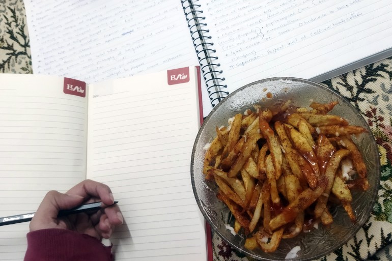 An overhead shot of a bowl of seasoned fries and two notebooks set up on a bed as Labanya studies and eats
