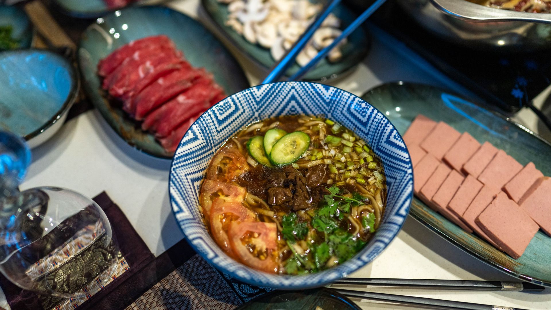 Overhead shot of a bowl of noodle soup topped with veggies and herbs and stir-fried beef