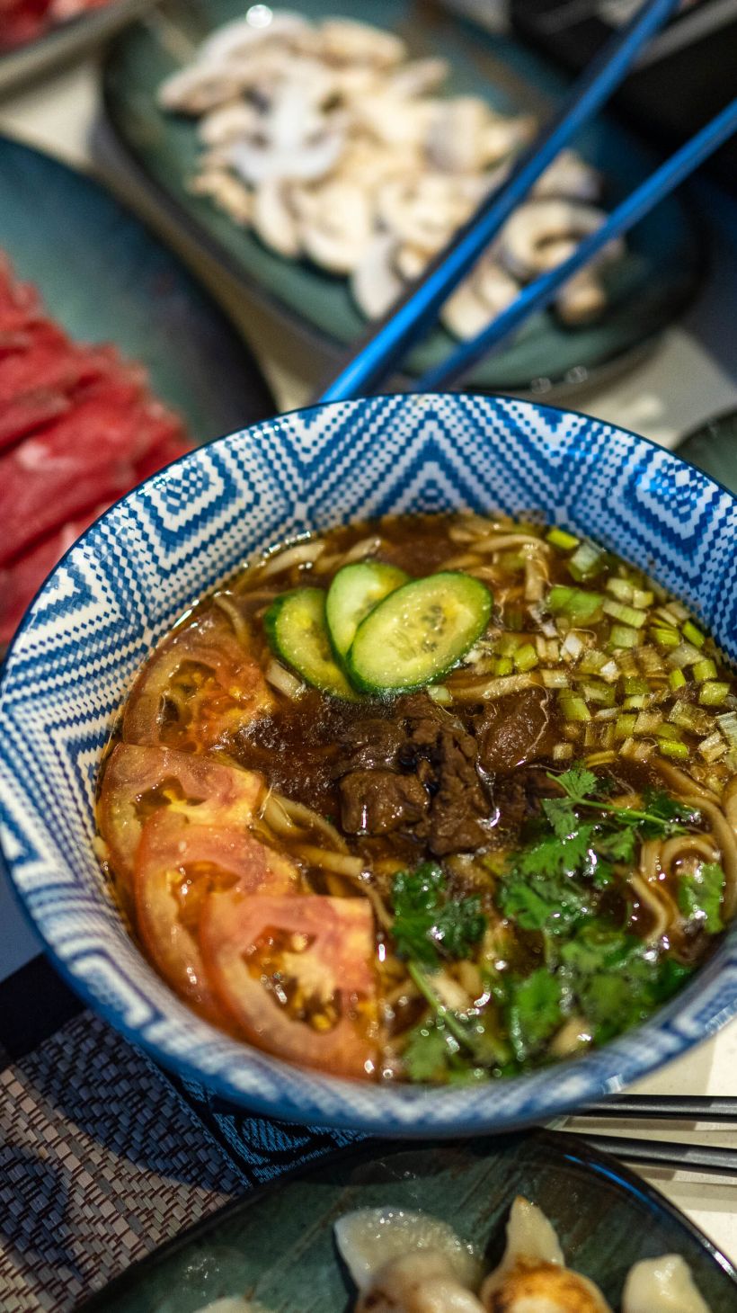 Overhead shot of a bowl of noodle soup topped with veggies and herbs and stir-fried beef