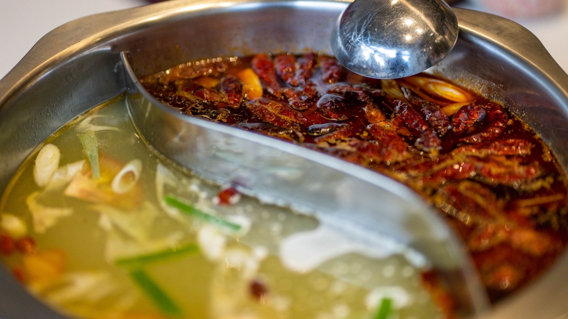 close view of the hotpot, one side is spicy, with chillis and peppers floating in the red broth, while the other is mild with veggies on a clear broth