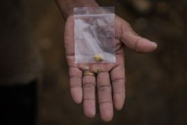 A miner shows a nugget of gold inside a small plastic bag on his calloused palm. He is wearing a wedding ring