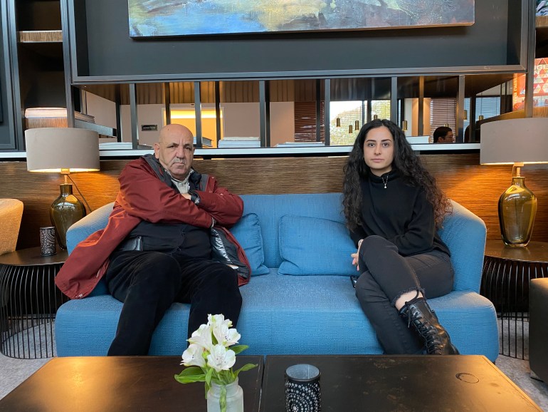 A photo of two people sitting next to each other on a sofa.