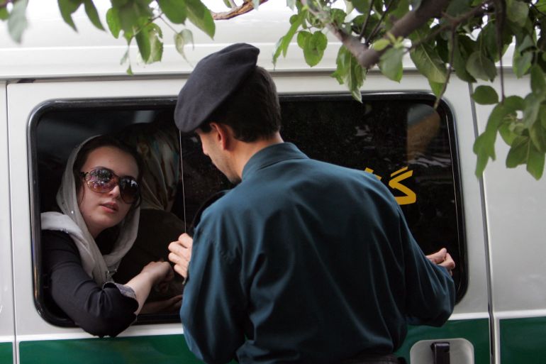 An Iranian policeman speaks with a woman in a police car after she was arrested because of her 'inappropriate' clothes