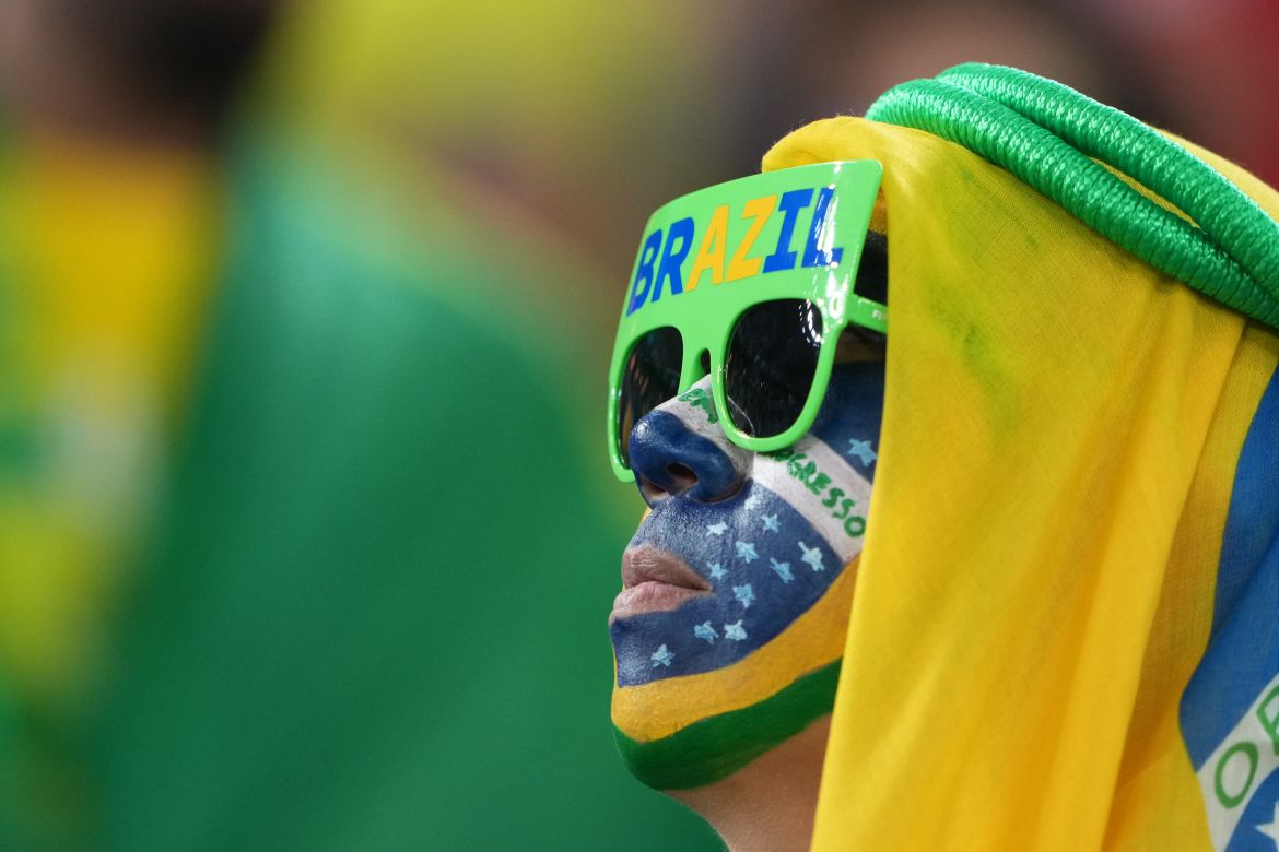 A Brazil fan looks on with their face painted in the colours of the Brazilian flag and wearing similar-coloured sunglasses.
