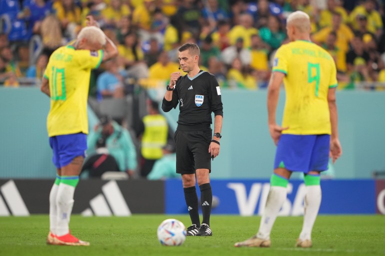 The referee has a word while two Brazilian players stand before him and wait.