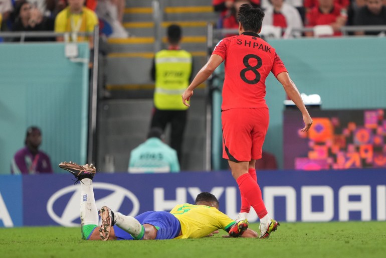 Paik Seung-ho in action for the Korean team; a Brazilian lies flat on the pitch in front of him.