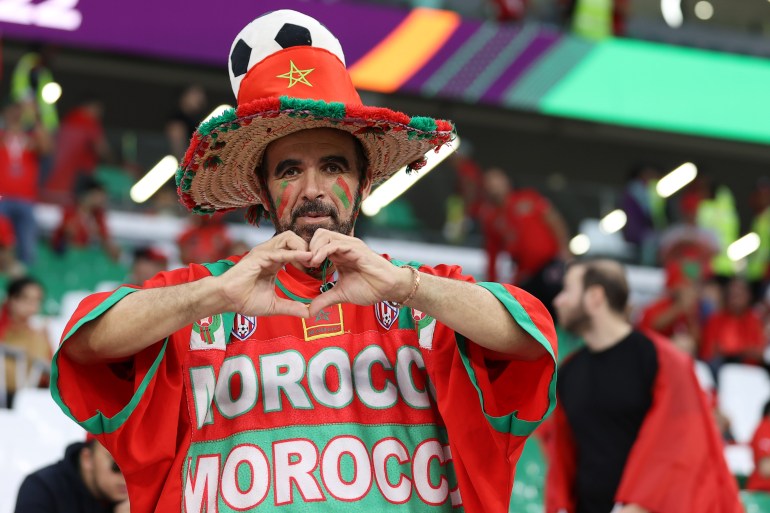 A fan in the stands, dressed in the colours of the Morrocan flag, makes a heart shape with his hands ahead of the game against Spain.