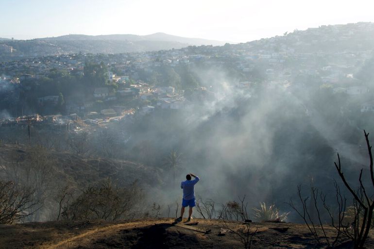 A man surveys the damage of a wildfire from a scorched hilltop