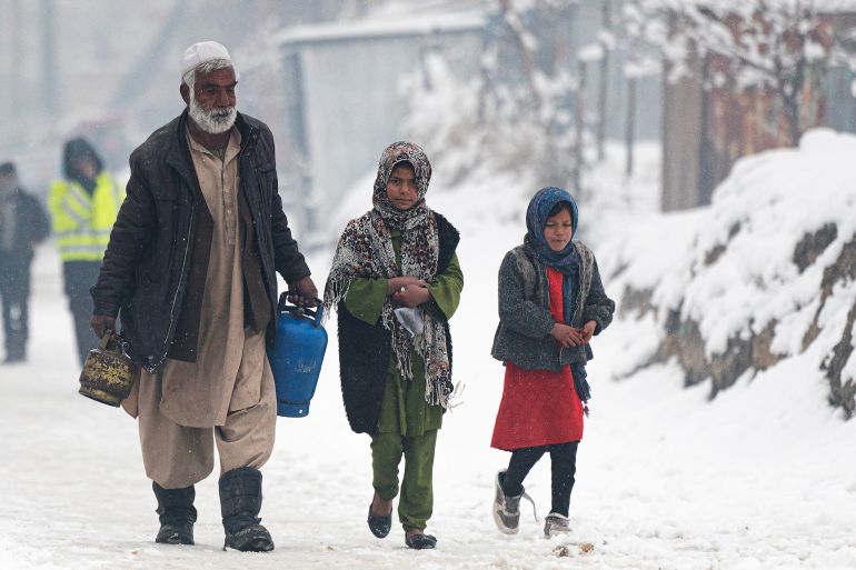 A man carrying gas canisters walks next to children along a street during snow fall in Kabul