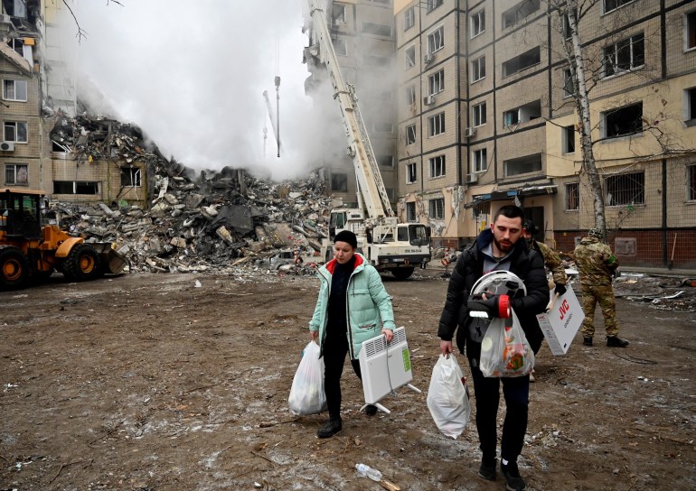 Residents carry their belongings from a residential building destroyed after a missile strike, in Dnipro on January 15, 2023.