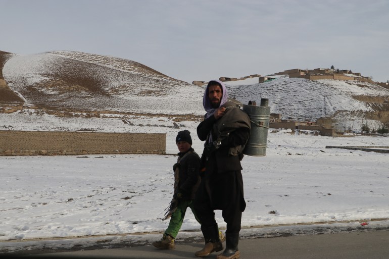 A man and boy walk along a road during a cold winter day in Yaftal Sufla district of Badakhshan Province on January 18, 2023. - At least 70 people have died in a wave of freezing temperatures sweeping Afghanistan, officials said on Janaury 18, as extreme weather compounds a humanitarian crisis in the poverty-stricken nation. (Photo by OMER ABRAR / AFP)