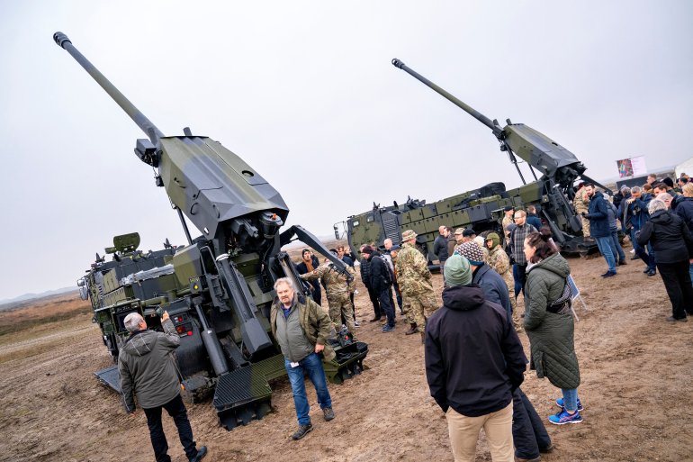 Two Caesar howitzer systems being displayed by the Danish army. Their guns are pointing towards the sky and there are men million about.