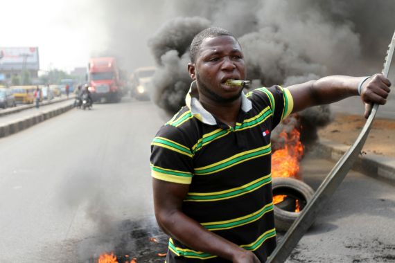 A protester walks past burning tyres while biting a lighter during a rally against fuel subsidy removal on Ikorodu road in Nigeria's commercial capital Lagos January 3, 2012. Hundreds of demonstrators in Nigeria's commercial capital Lagos shut petrol stations, formed human barriers along motorways and hijacked buses on Tuesday in protest against the shock doubling of fuel prices after a government subsidy was removed. REUTERS/Akintunde Akinleye (NIGERIA - Tags: CIVIL UNREST POLITICS ENERGY)