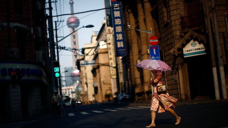 A woman walks across a Shanghai street with an umbrella to protect herself from the sun.