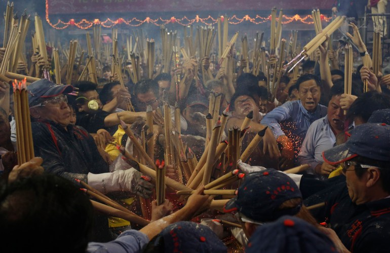 People crowd around an urn in a Chinese temple in Singapore clutching their joss sticks. They want to be the first to plant their stick in the year. They look c
