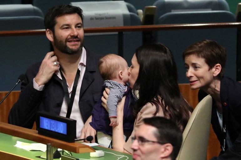 Jacinda Ardern kisses baby Neve in the chamber of the UNGA. Her partmer is next to her and other people are looking at the baby. Everyone looks happy.