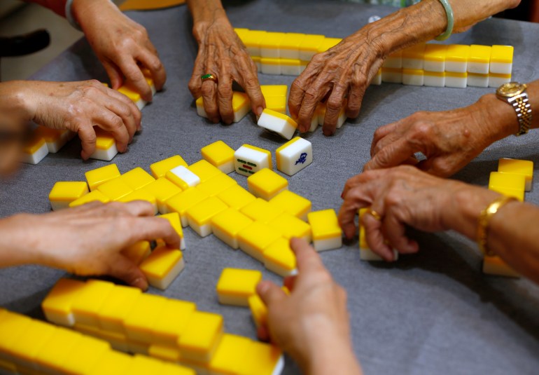 A close up of yellow mahjong tiles and the hands of the four people playing the game