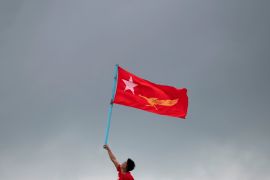 A supporter holds an NLD flag high in the air. The flat is red with yellow markings and stands out against the grey sky