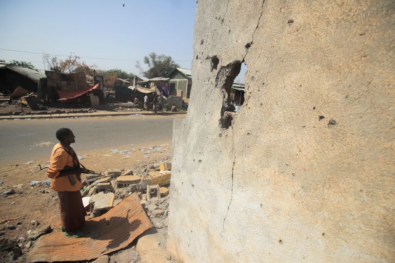 An armed militia stands next to a house damaged during the fight between the Ethiopian National Defence Forces (ENDF) and the Tigray People's Liberation Front (TPLF) forces