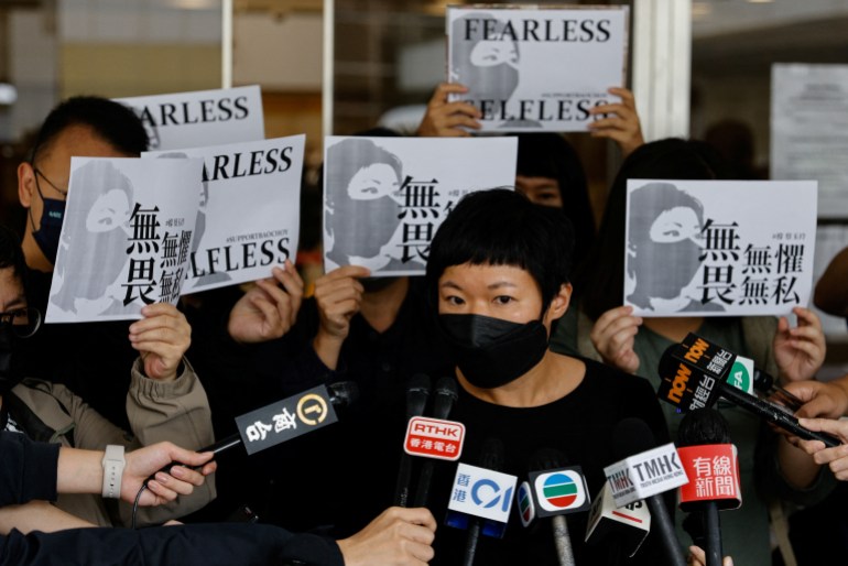 Journalist Bao Choy speaking to the media outside court. She is wearing a black face mask. People behind her are holding up signs reading 'Fearless'.