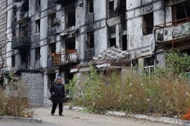 A woman walks past a damaged building in Mariupol