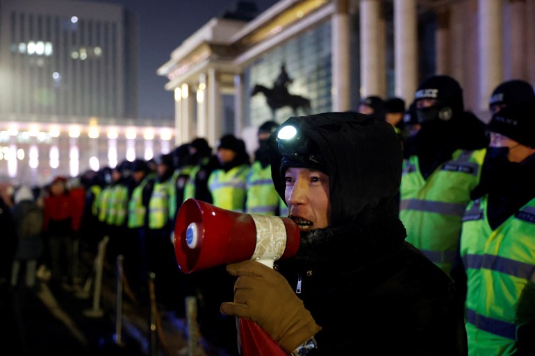A protester in Mongolia with a small megaphone is standing in front of a line of police officers wearing high-vis vests.