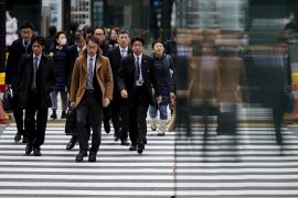 People crossing the road in Tokyo. Most are men, in suits. There are a few women.