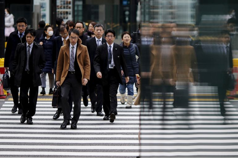 People crossing the road in Tokyo, Japan. Most are men in suits but there are a few women.