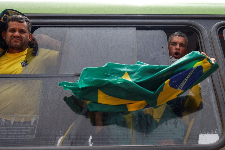 A man holds a Brazilian flag from the window of a bus as he is detained
