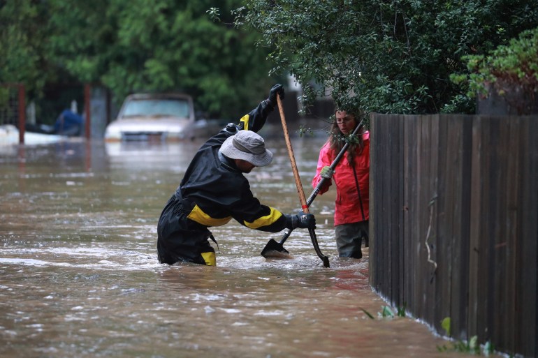 Pete Dal Ferro and Melissa Foley work to clear debris in their neighborhood as the San Lorenzo River rises with emergency evacuation orders in Felton Grove, California, U.S., January 14, 2023. 