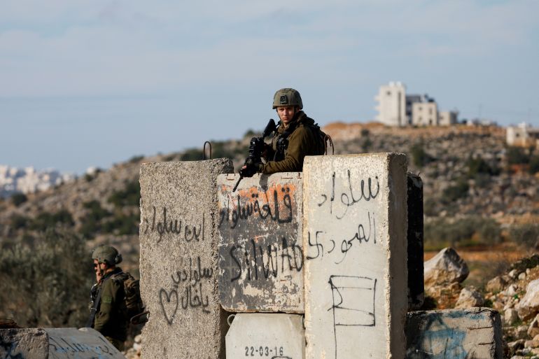Israeli soldier stands behind a concrete barricade holding a gun