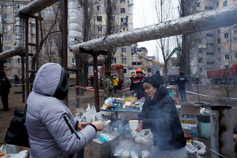 A woman distributes food as emergency personnel work at the site where an apartment block was heavily damaged by a Russian missile strike