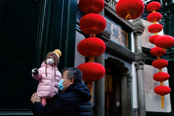 An elderly person holds a child near lanterns decorating a shop in Beijing, China.