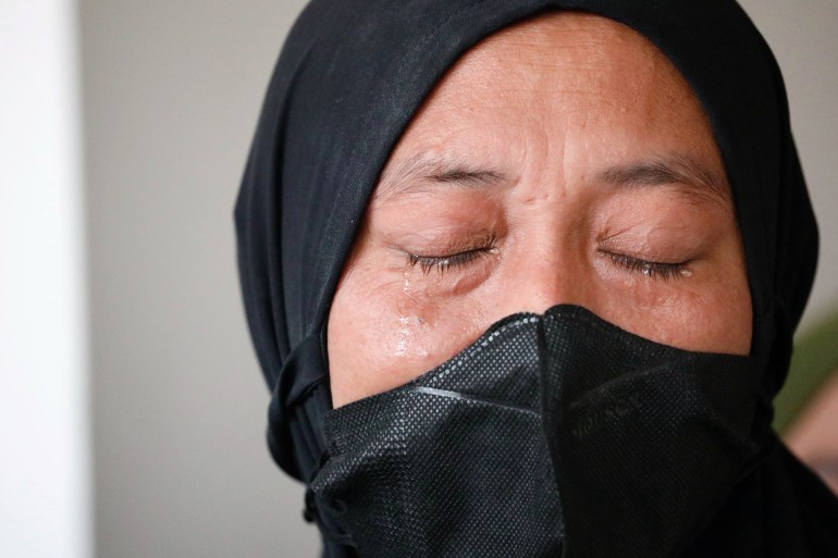 A close up of Desi Permata Sari taken in court. She has her eyes closed and tears are trickling down her cheeks. She is wearing a black headscarf and a black face mask