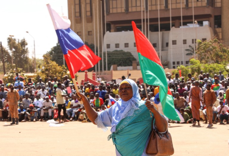 A woman holds her national flag and the Russian flag as people gather to show their support for Burkina Faso's new military leader Ibrahim Traore.