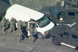 Armed police in combat uniforms swoop on a white van in Torrance, California. The van is surrounded by armoured vehicles with the word Sheriff on the side.