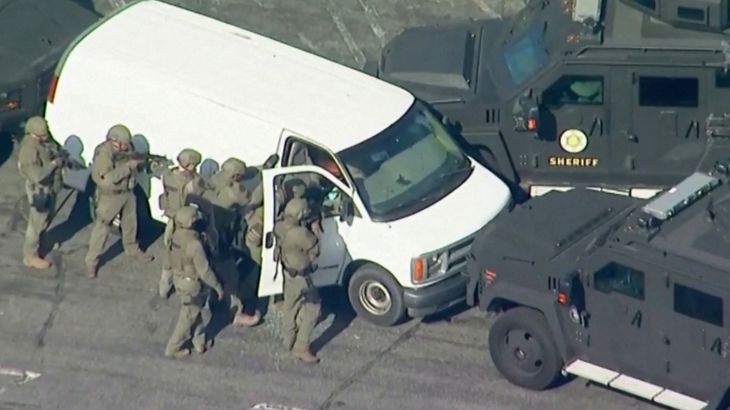 Armed police in combat uniforms swoop on a white van in Torrance, California. The van is surrounded by armoured vehicles with the word Sheriff on the side.