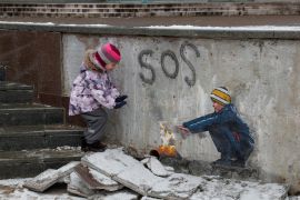 Two children play in rubble next to artwork on a street in Bucha, Ukraine.