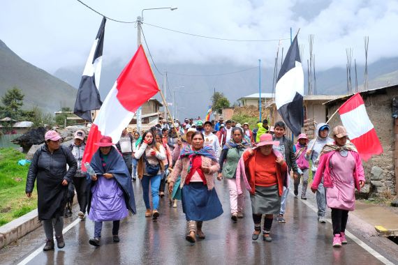 Protesters under a cloudy sky carry flags and walk down a street in protest in Peru.
