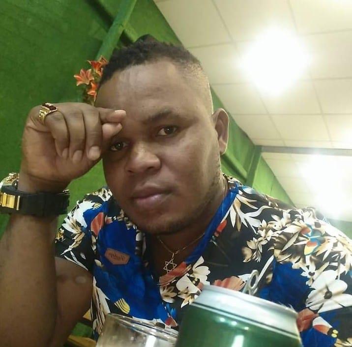 Christopher Osinanna Nwadik wearing a floral shirt and has his hand at his forehead.