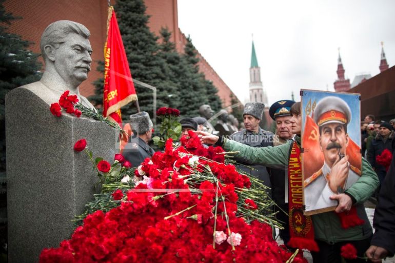 A woman holding a portrait of Stalin places flowers near the monument signifying Joseph Stalin's grave near the Kremlin wall marking the anniversary of Stalin's birth in Moscow's Red Square, Russia, Thursday, Dec. 21, 2017. (AP Photo/Alexander Zemlianichenko)