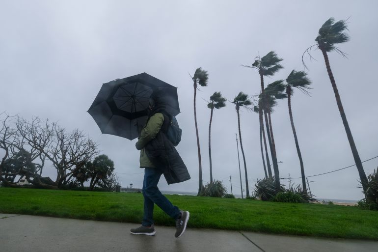 A woman walks with wind-beaten umbrella in California