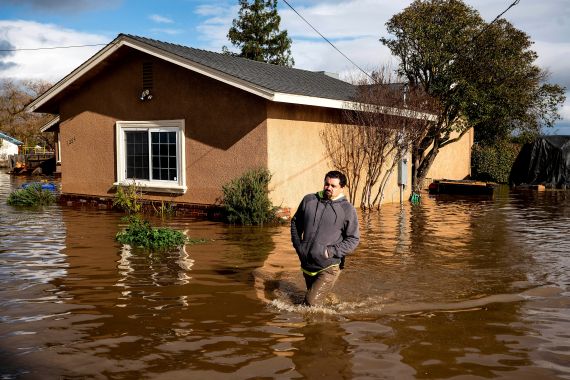 A man trudges through floodwaters in Merced, California, in front of a sandy-coloured house